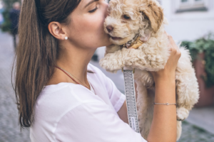 A woman affectionately kisses her dog while standing on a city street.