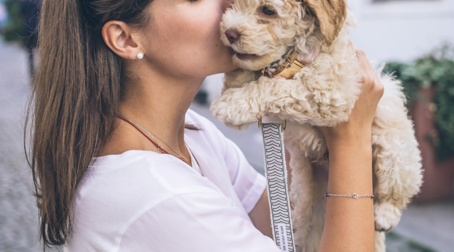 A woman affectionately kisses her dog while standing on a city street.